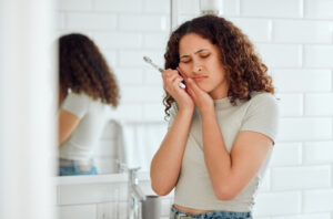 Toothache, pain and sensitive teeth with a woman brushing her teeth in a bathroom at home. Young fe