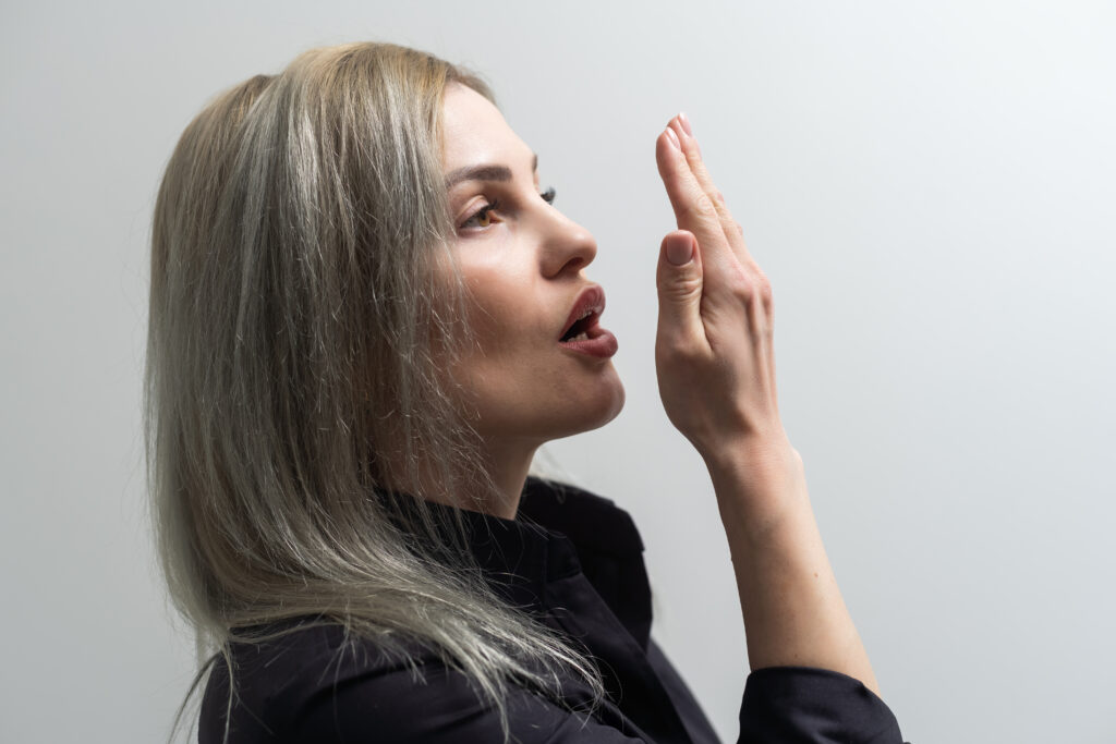 young woman checking her breath with her hand